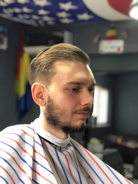 Bărbat cu barbă și tunsoare pieptănată pe spate, după tuns