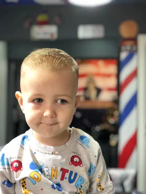 Băiețel cu tunsoare scurtă, lângă barber pole