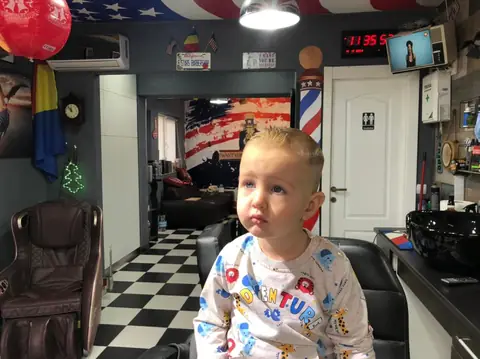 Băiețel cu tunsoare scurtă, cu muralul american în fundal