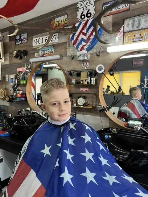 Băiat blond zâmbitor după tuns, în salon
