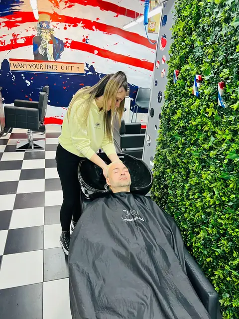 Frizerița spălând părul unui client, lângă peretele verde