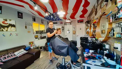 Frizerul tunzând un client sub tavanul cu steag american