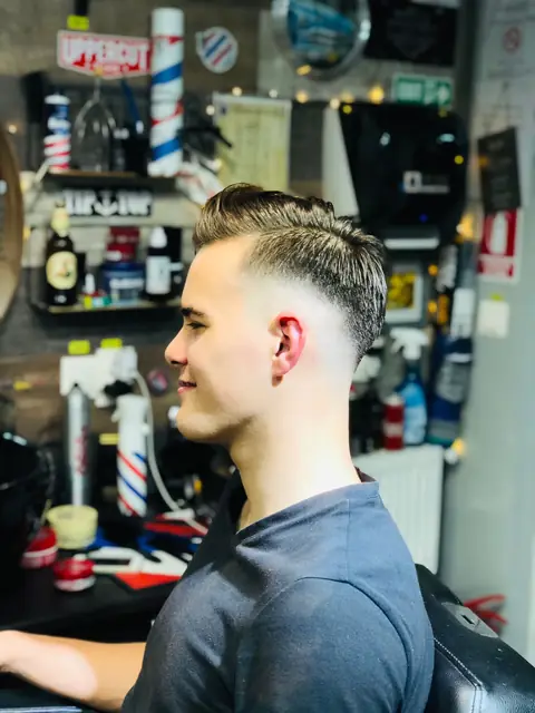 Tânăr cu fade și păr pieptănat pe spate, din profil